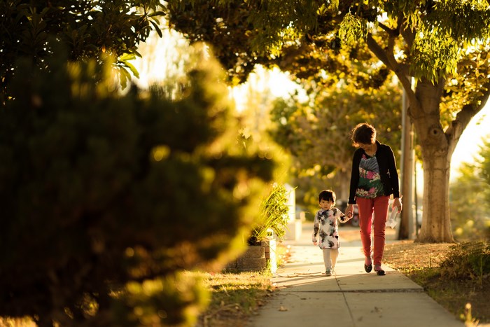 Woman and child walking on sidewalk at sunset