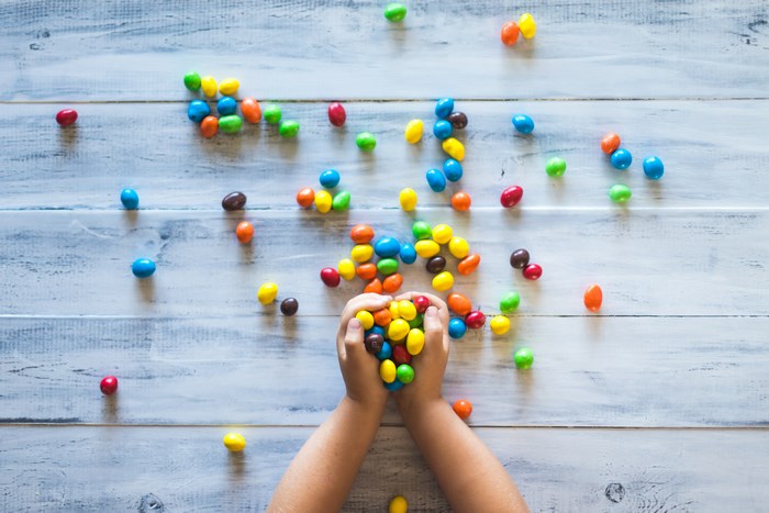 Child's hands holding colorful M&Ms on a wooden surface