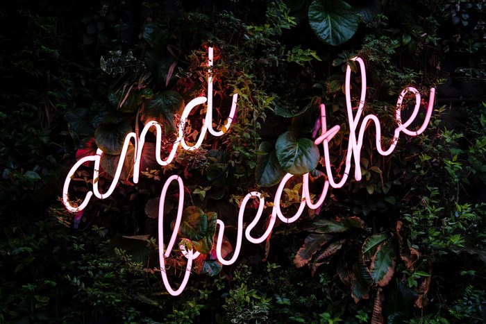 Pink neon sign 'and breathe' on a green wall