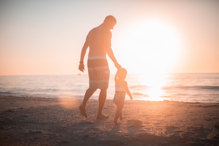 Father and child walking on beach at sunset