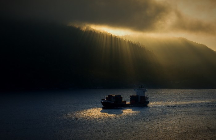 Cargo ship sailing through sunbeams on the water