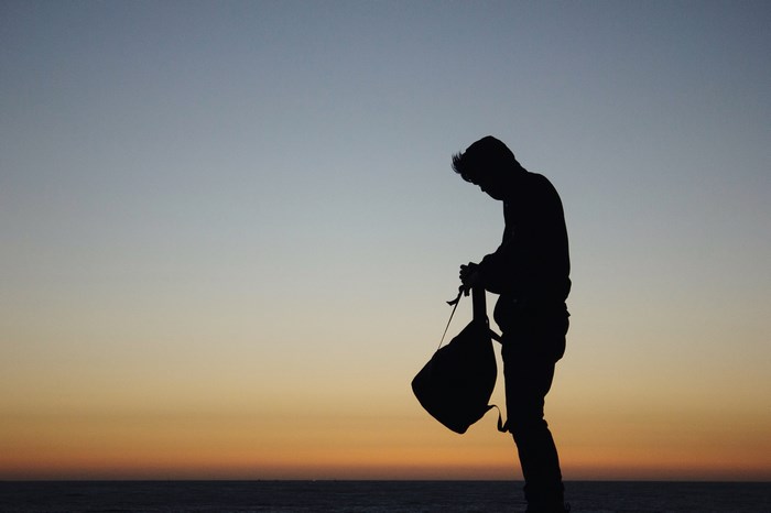 Silhouette of a man holding a backpack at sunset