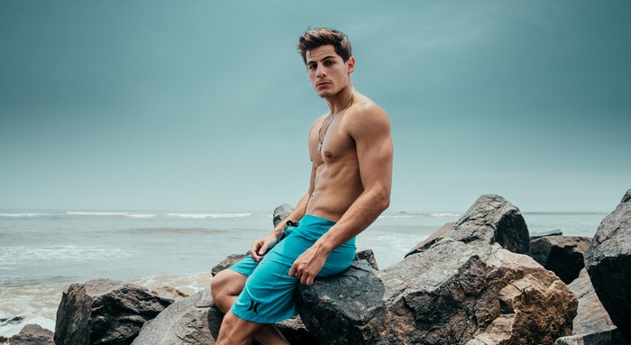Man in blue shorts sitting on rocks by the ocean