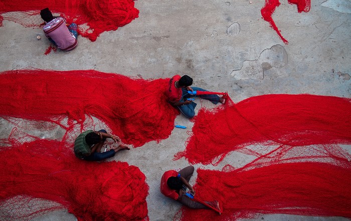Men working with red fishing nets on a concrete floor