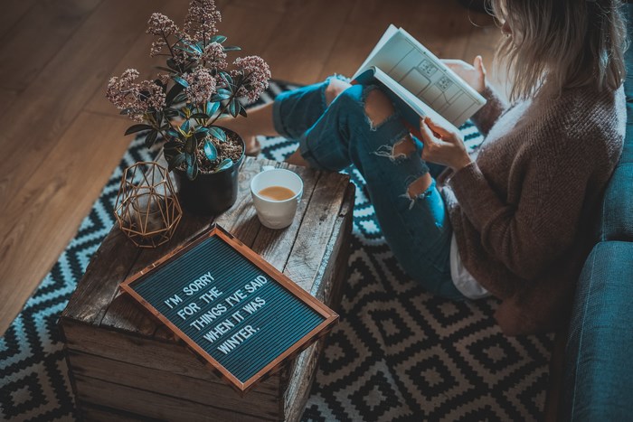 Woman reading a book with a message board and plant