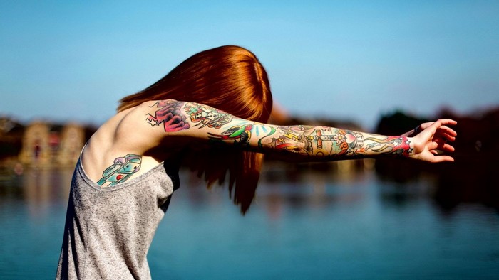 Woman with full arm tattoos by the water