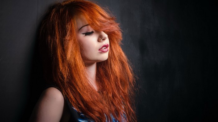 Redhead woman leaning against a dark wall