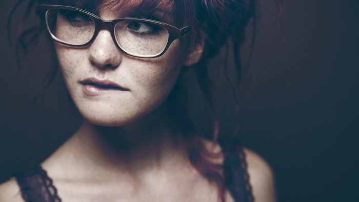 Redhead woman with freckles and glasses biting lip