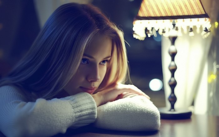 Woman resting head on arms near lamp