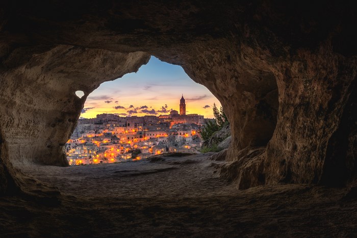 Cave entrance overlooking Matera cityscape at sunset
