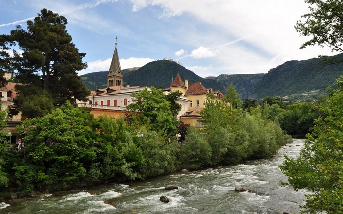 River flowing through a town with a church steeple and mountains