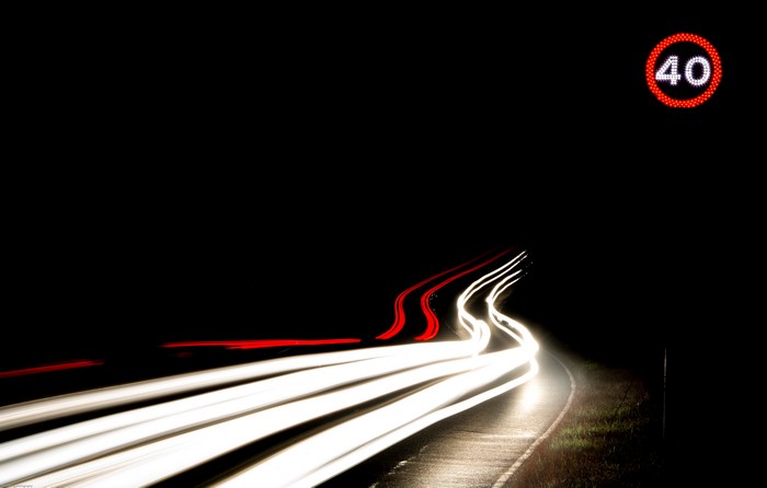 Long exposure of car lights on a road at night with speed sign