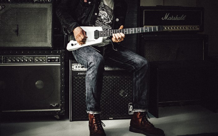 Man playing a white guitar on top of amplifiers