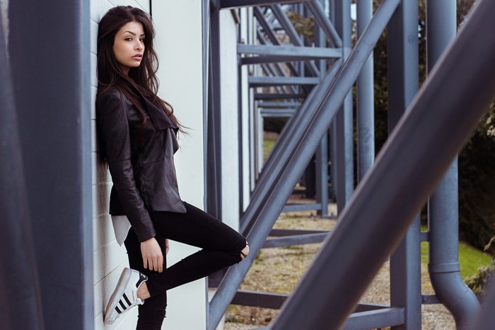 Woman in leather jacket and ripped jeans posing by metal structure
