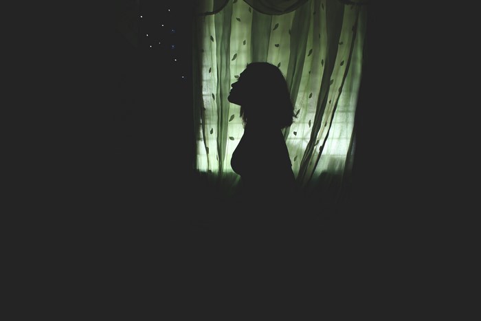 Silhouette of a woman by a window with curtains
