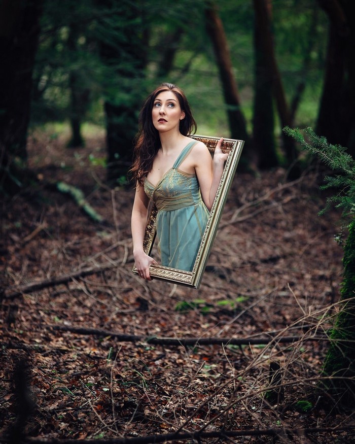Woman in blue dress holding a picture frame in forest