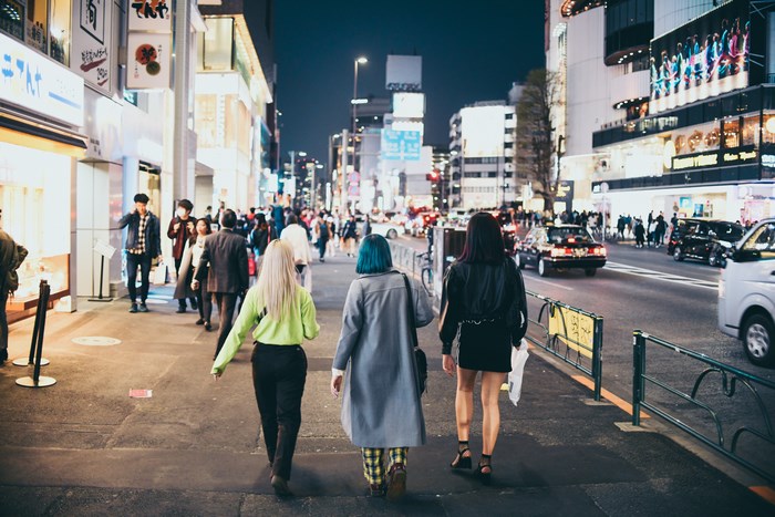 Three young women walk down a busy city street at night.