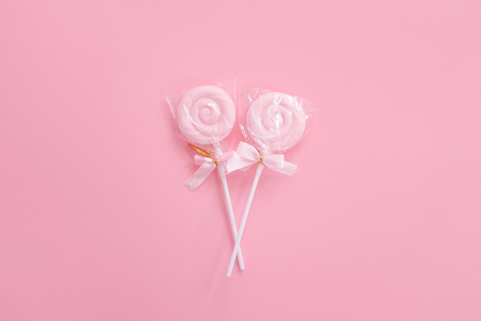 Two pink swirl lollipops with bows on pink background