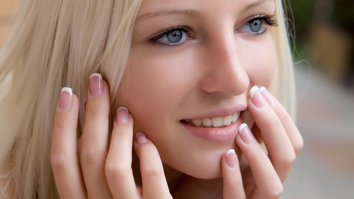 Woman with blonde hair and blue eyes, hands near face