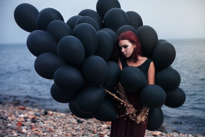Woman with black balloons on a rocky beach