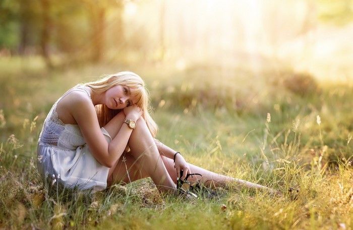 Blonde woman sitting in a grassy field at sunset