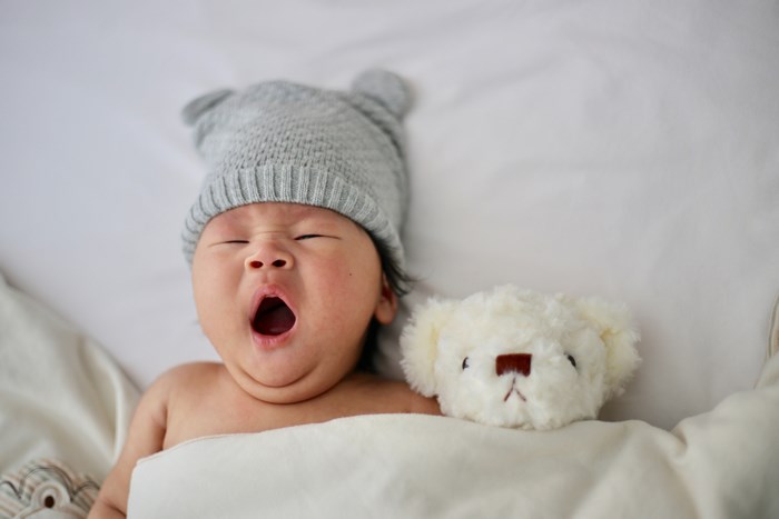Newborn baby yawning next to a teddy bear