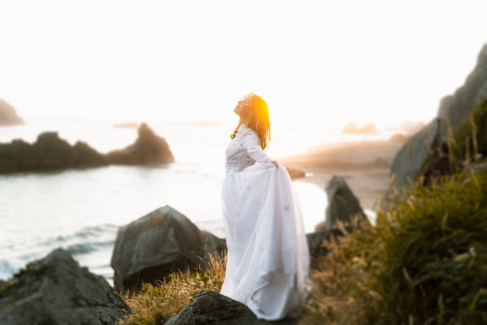 Woman in white dress on rocky coast at sunset