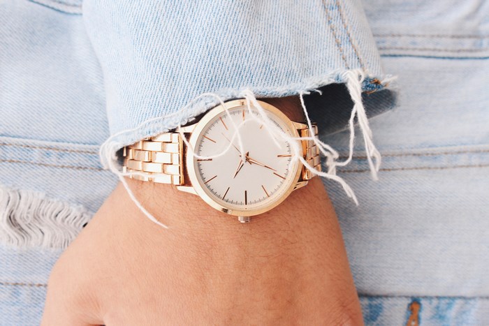 Close-up of a gold watch on a wrist under a denim jacket