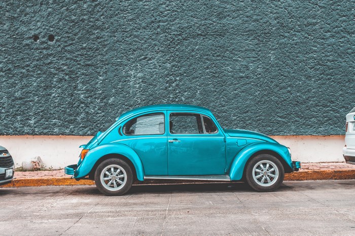 Teal Volkswagen Beetle parked by a textured wall