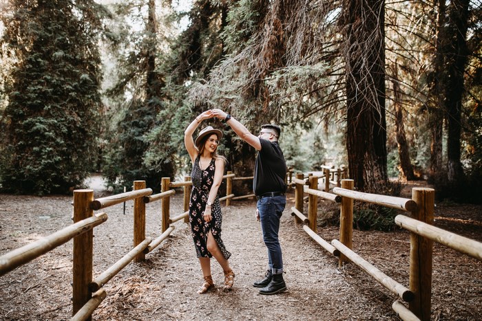 Couple dancing on a forest path with a wooden fence