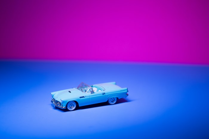 Blue vintage convertible toy car on a blue and pink background