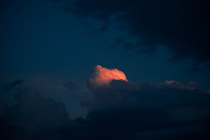 Pink cloud illuminated by sunset against dark blue sky