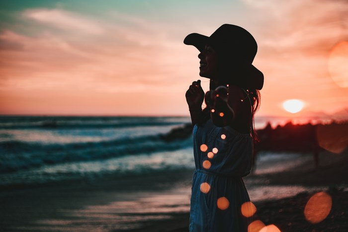 Woman in hat with fairy lights at sunset on beach