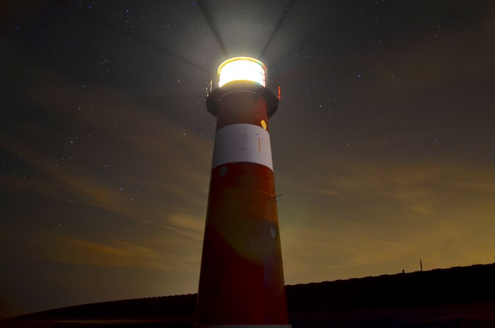 Lighthouse shining light at night with stars