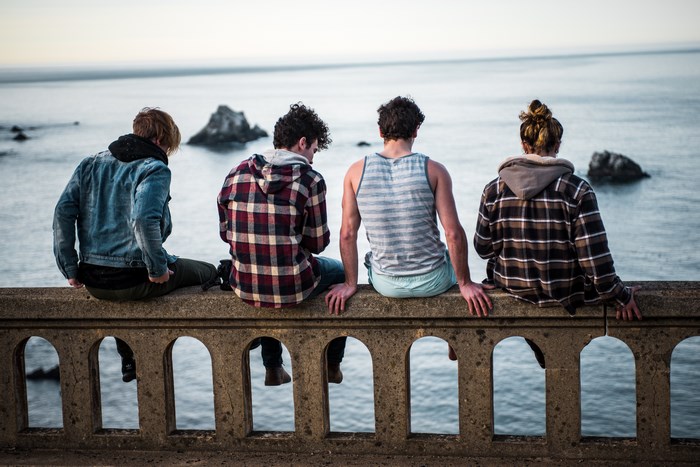 Four friends sitting on a bridge overlooking the sea