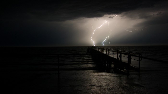 Lightning strikes over a pier at sea during a storm