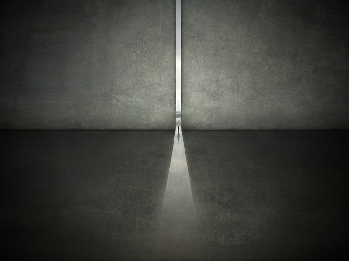 Two men walk through a narrow opening in a concrete wall.