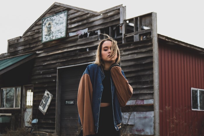 Woman in a denim and brown jacket outside an abandoned barn