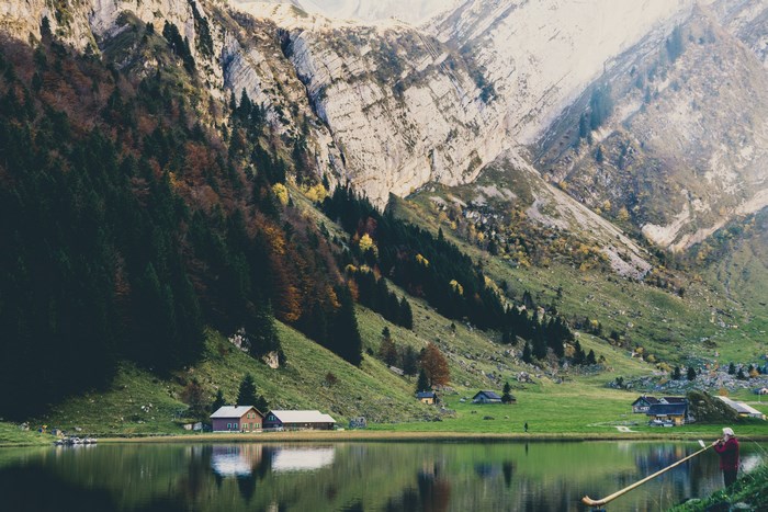 Man plays alphorn by a lake in the Swiss Alps