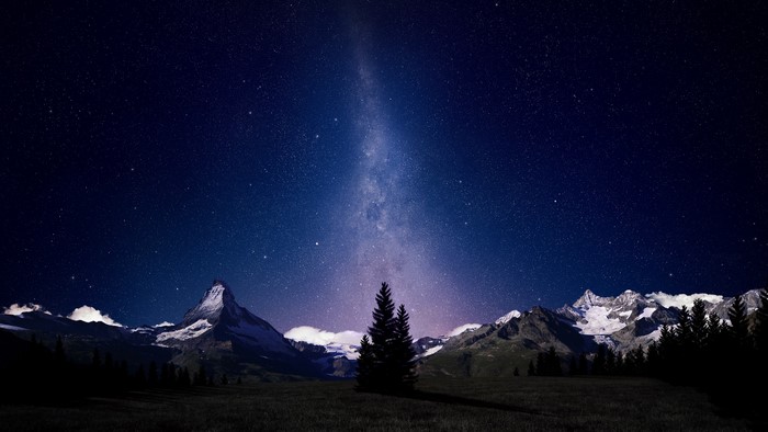 Starry night sky over snow-capped mountains and trees