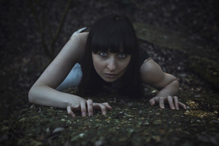 Woman crawling on the ground in a dark forest