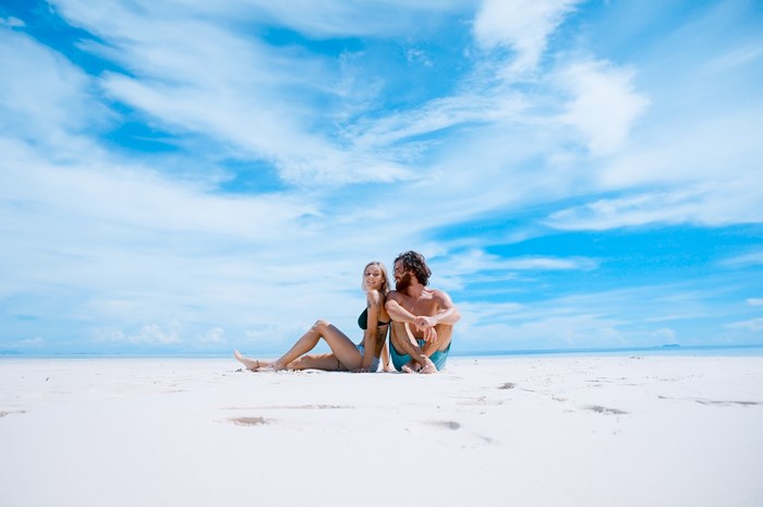 Couple sitting on a white sand beach under a blue sky