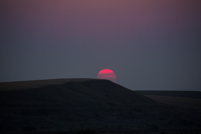 Red sun setting over dark hills at dusk