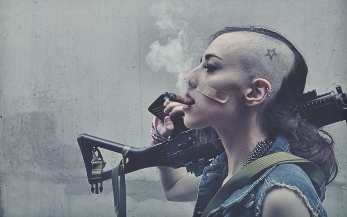 Woman with shaved head smoking cigar holding rifle