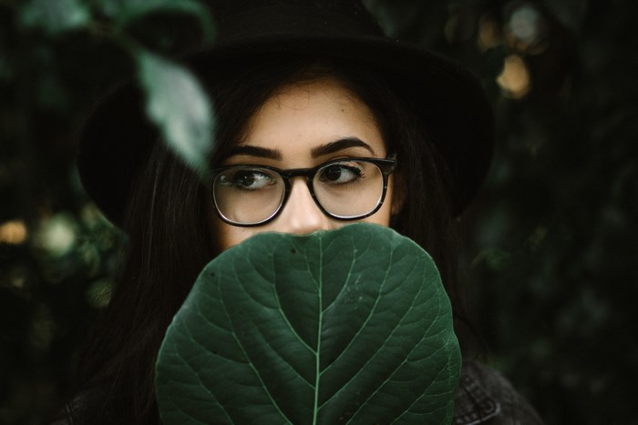 Woman wearing glasses and hat holding a leaf