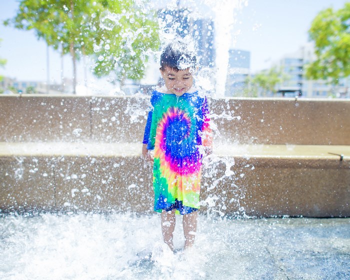 Child playing in a fountain with a tie-dye shirt