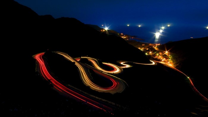 Night road with light trails and coastal town