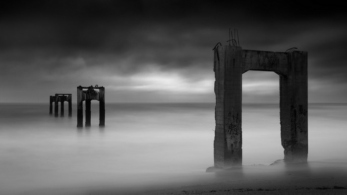 Ruined concrete pillars on a beach with long exposure sea and clouds