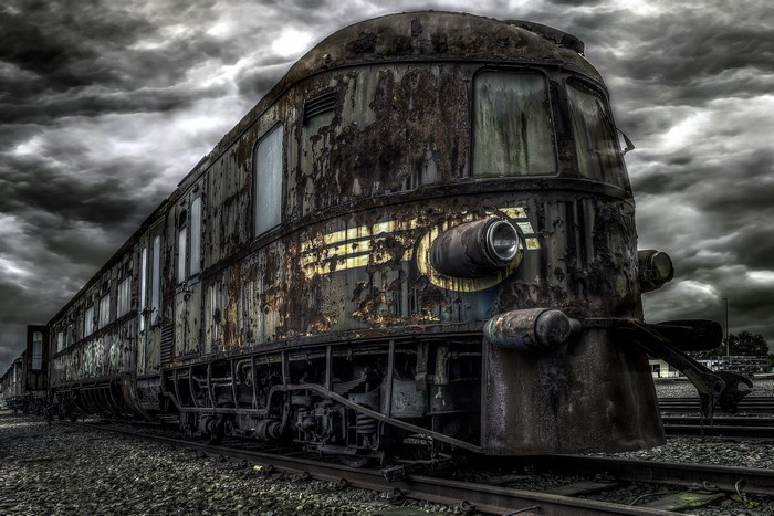 Abandoned rusty train on railway tracks under overcast sky