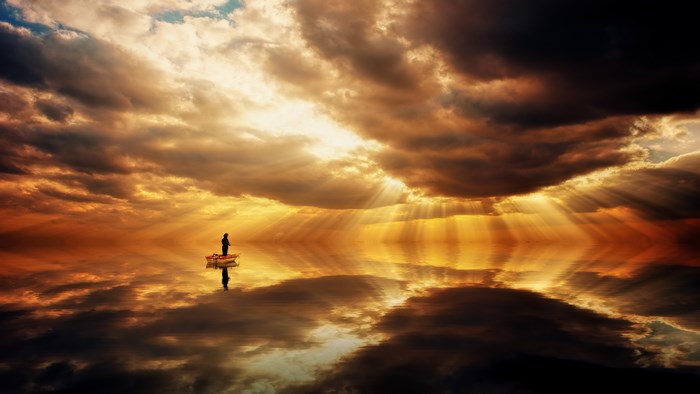 Man fishing in a boat at sunset with sun rays
